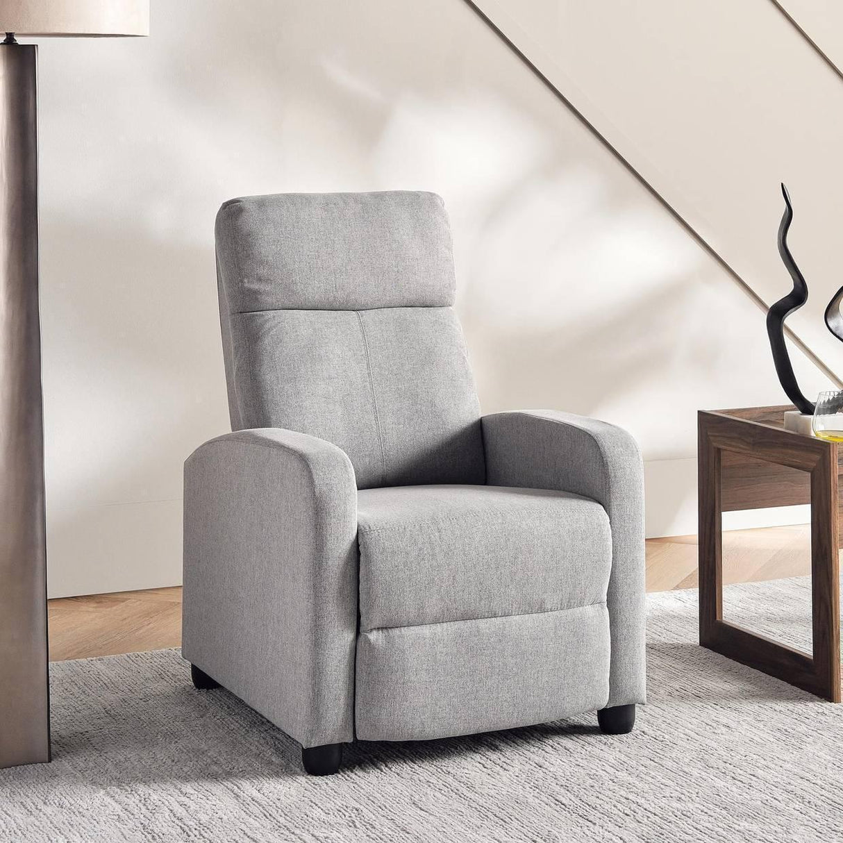 Modern gray fabric recliner chair in a living room with wooden side table and decor