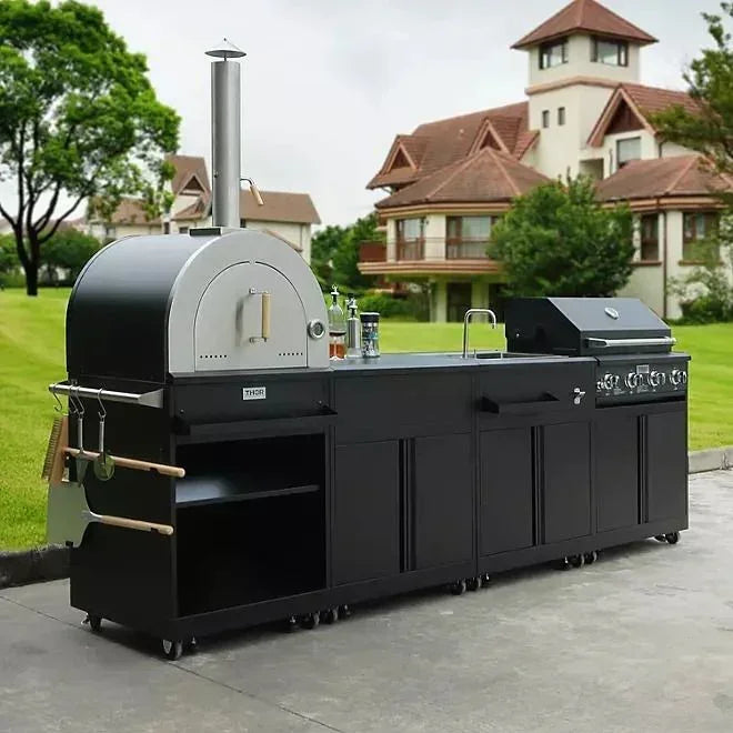 Outdoor black kitchen island with pizza oven and grill on patio, luxury home in background