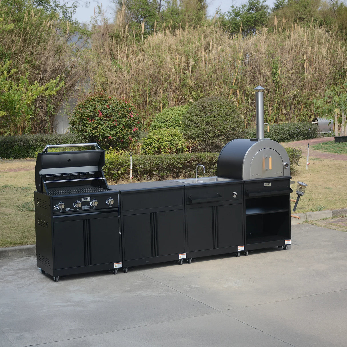 Outdoor black modular kitchen with gas grill, sink, and pizza oven on a patio