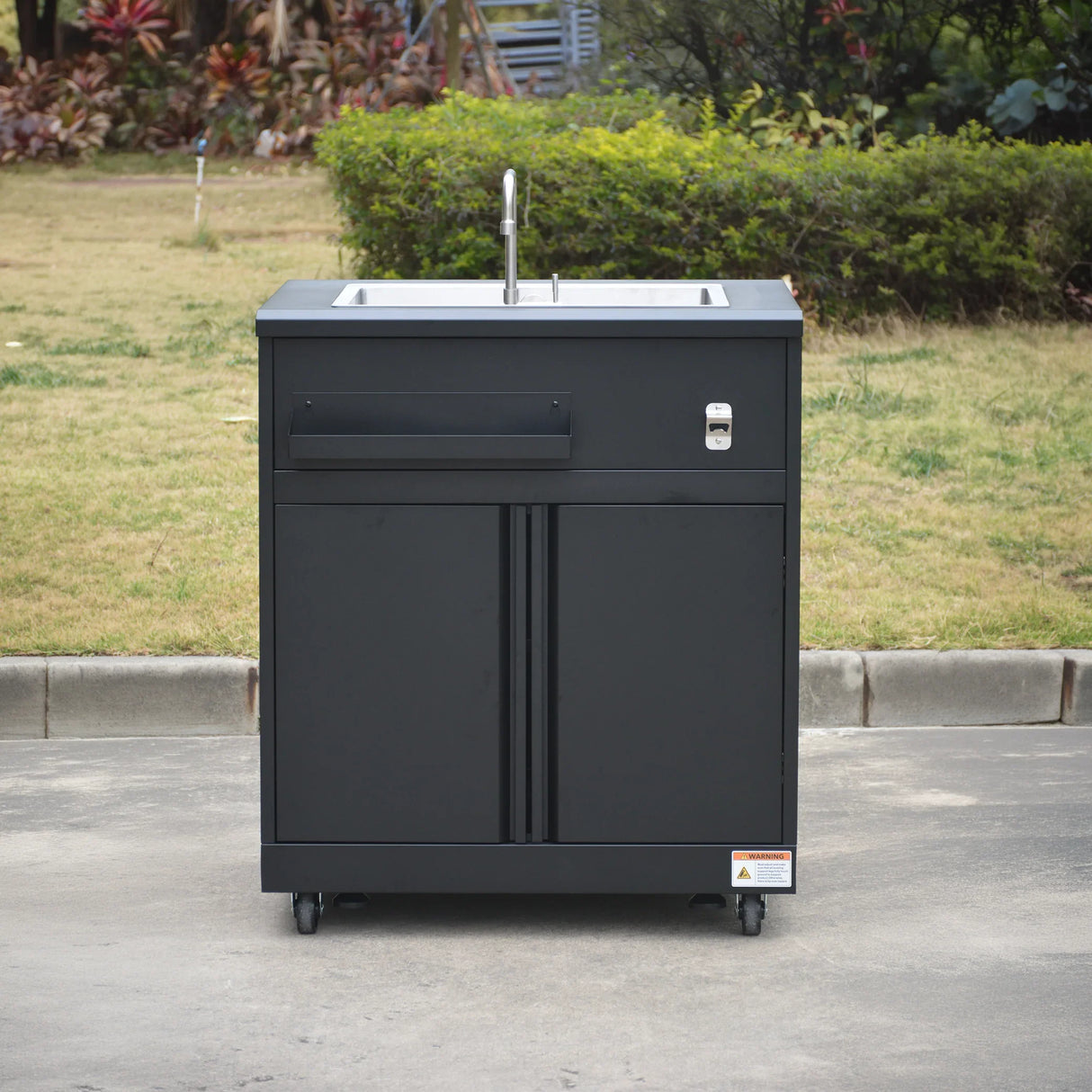 Outdoor black portable sink cabinet with faucet and storage, on wheels, in garden setting