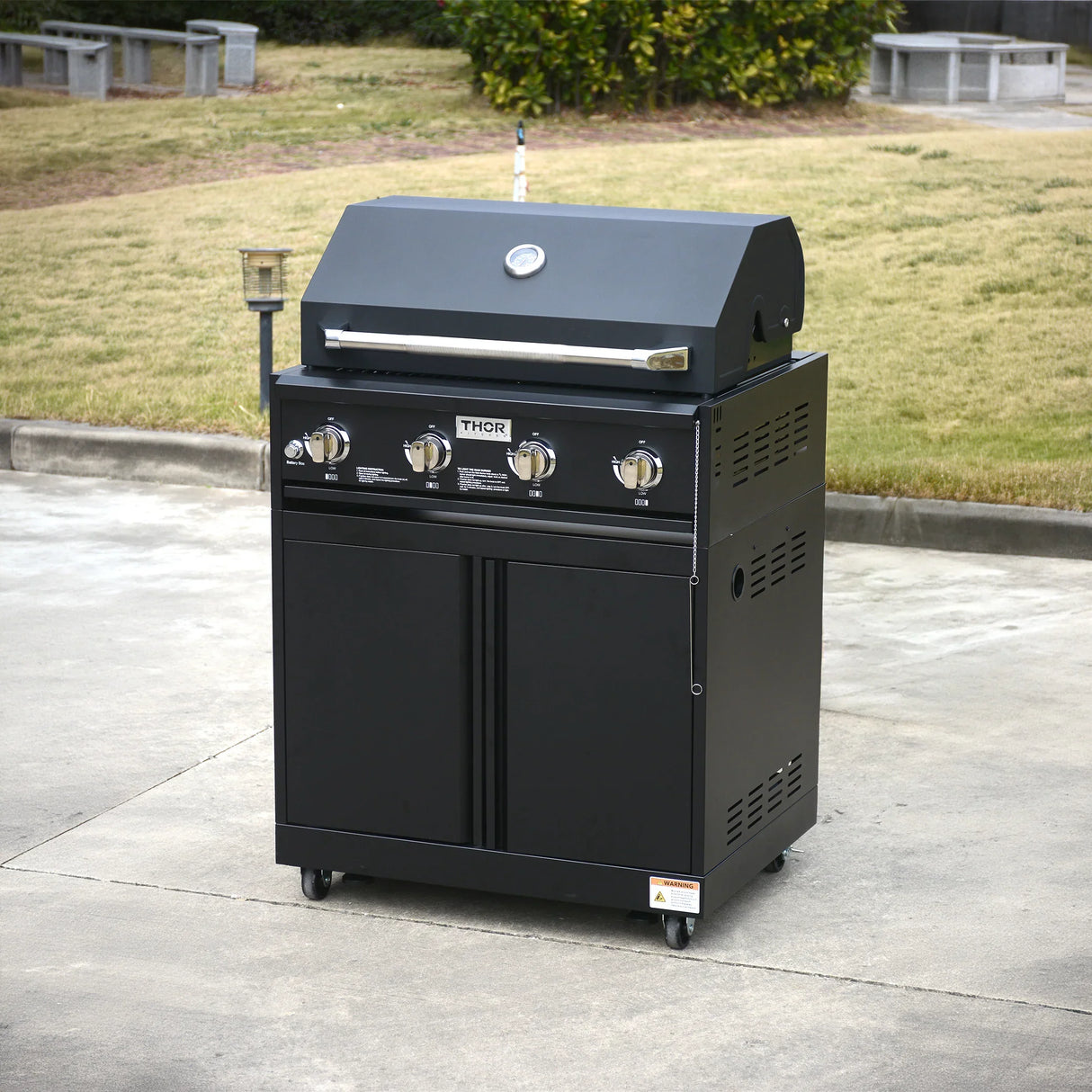 Outdoor black gas grill with four control knobs on wheels, placed on a patio