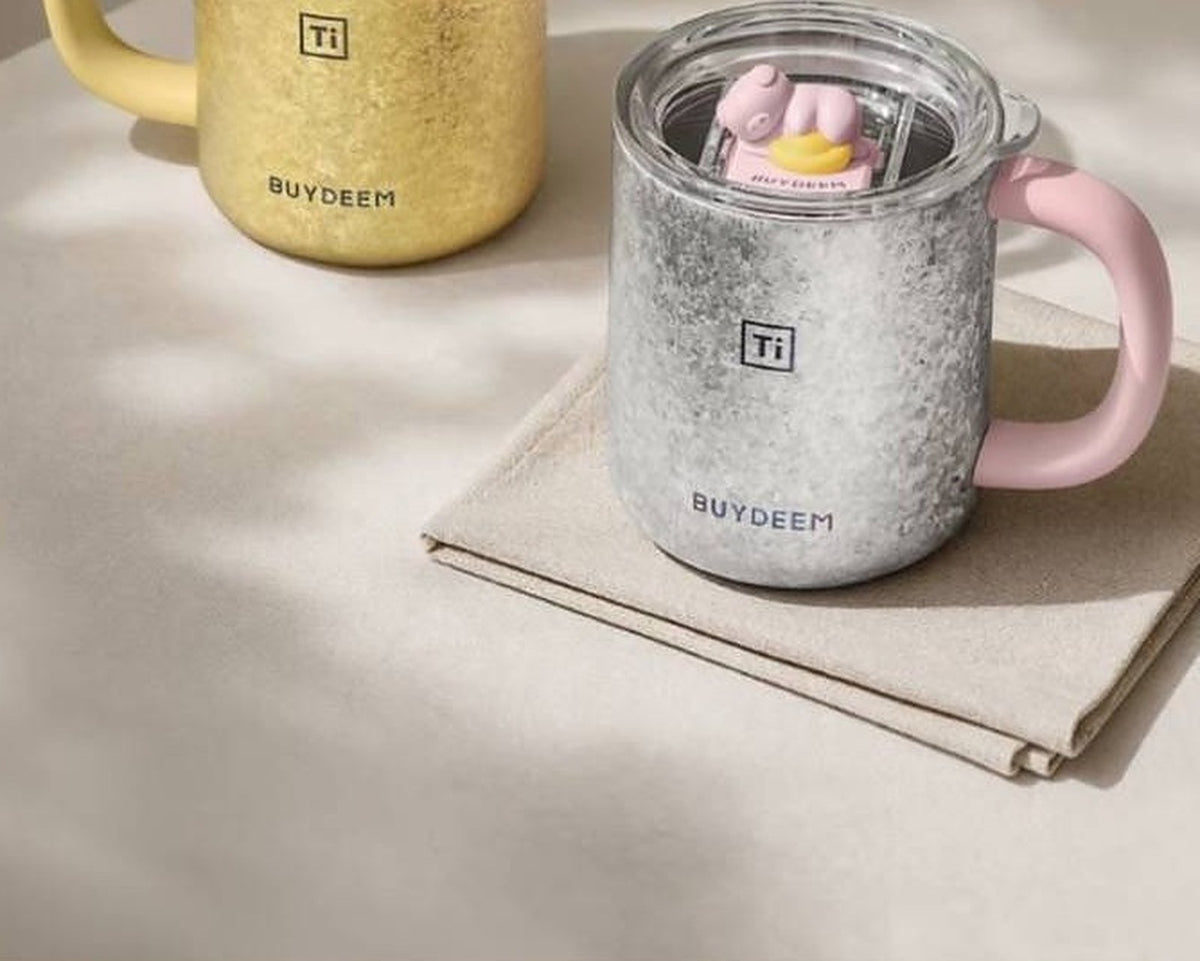 BUYDEEM T502 Pure Titanium Insulated Mug with Lid 430ml – silver pig mug on linen napkin, gold duck mug behind