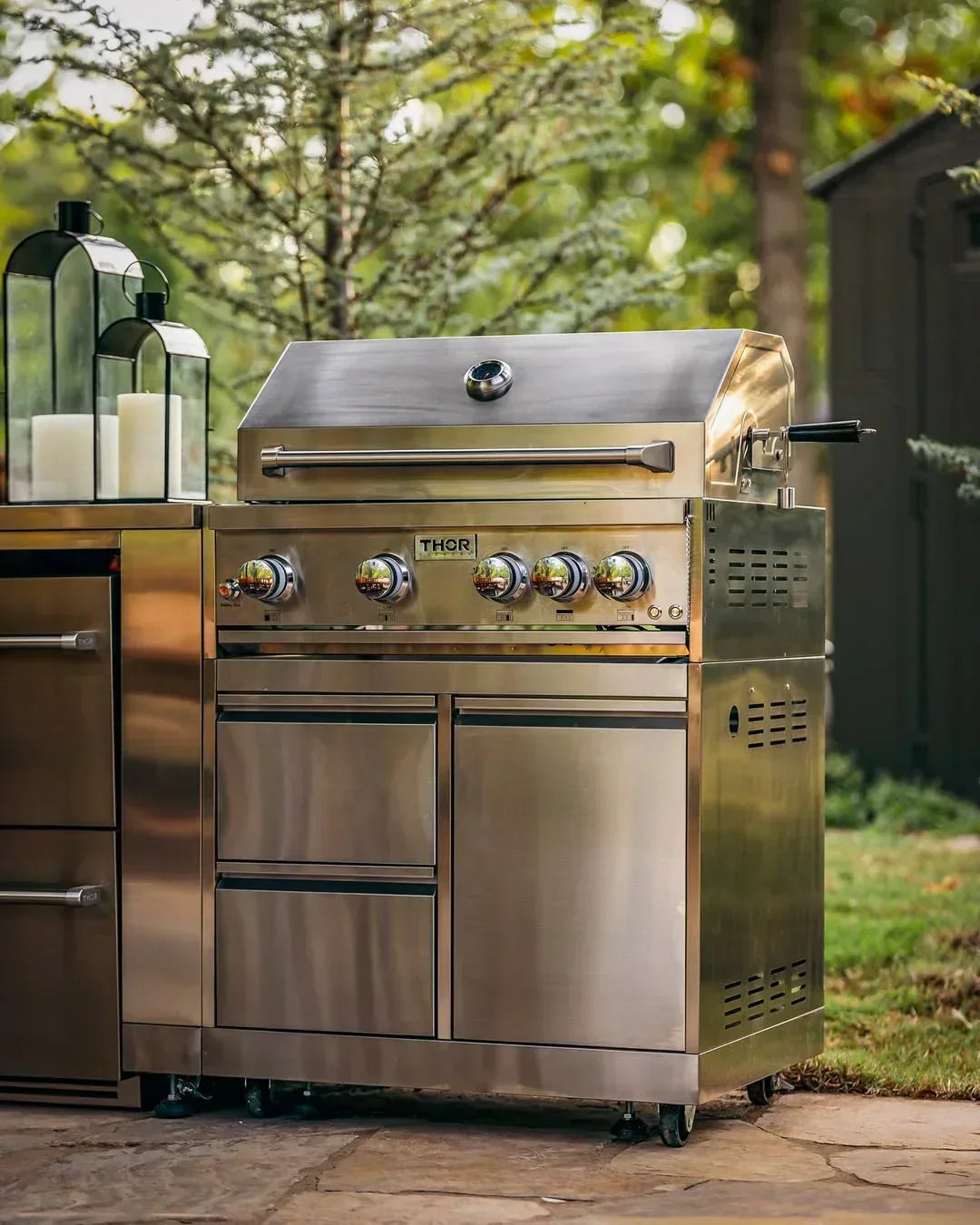 Stainless steel THOR outdoor gas grill with five control knobs and built-in thermometer on patio