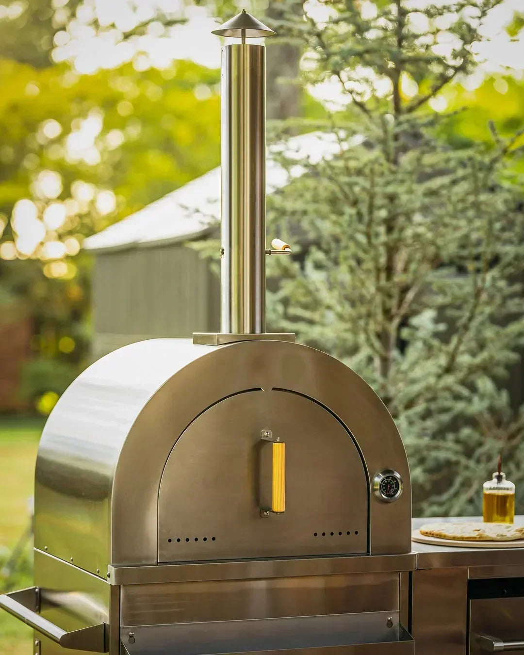 Stainless steel outdoor pizza oven with chimney and thermometer in backyard setting