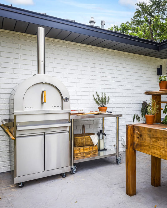 Outdoor pizza oven and stainless steel storage cabinet on a modern patio, white brick wall backdrop