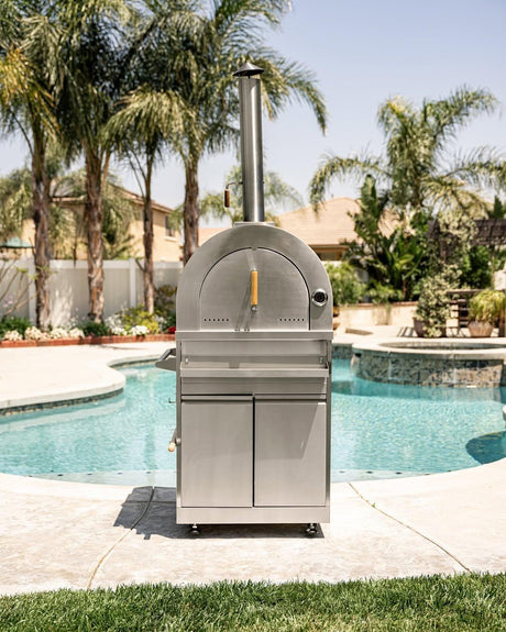 Modern stainless steel outdoor pizza oven by swimming pool with palm trees and sunny backyard