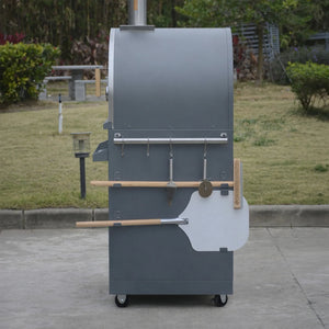Outdoor wood-fired pizza oven with tools on wheels in a garden setting