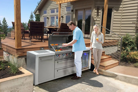 Man grilling at modern outdoor kitchen with stainless steel grill and refrigerator on patio