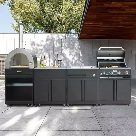 Modern outdoor kitchen setup with black cabinets, pizza oven, sink, and gas grill on patio
