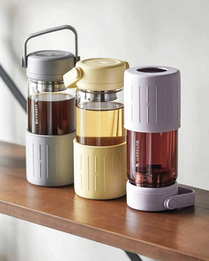 BUYDEEM DG45 Glass Tea Tumbler with Titanium Infuser 470ml – grey, yellow and lilac tumblers on a wooden shelf