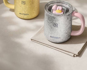 BUYDEEM T502 Pure Titanium Insulated Mug with Lid 430ml – silver pig mug on linen napkin, gold duck mug behind
