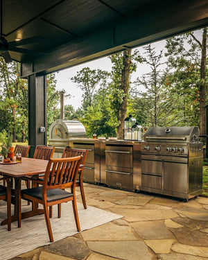 Modern outdoor kitchen with stainless steel grill, pizza oven, wood dining set on stone patio