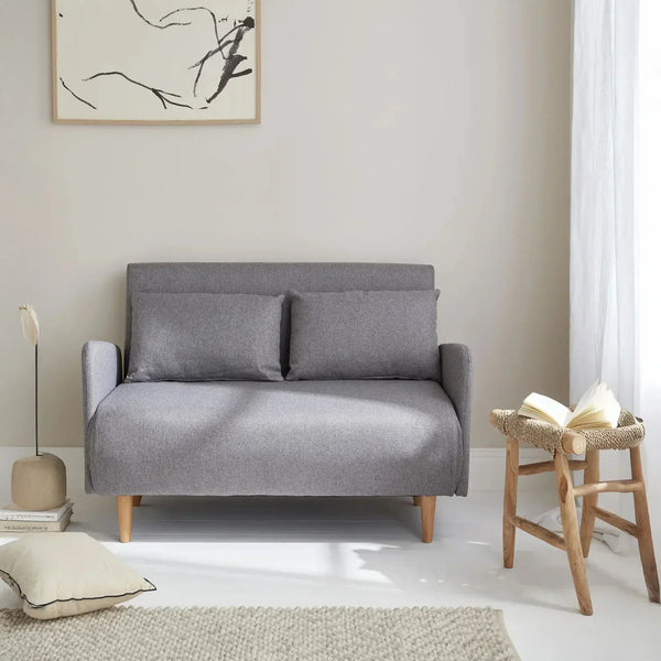 Modern grey sofabed in minimal living room with wooden legs and cozy decor